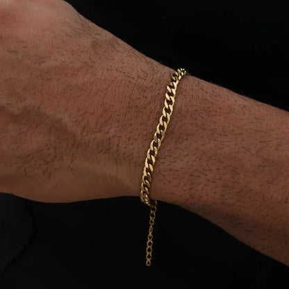 Gold-tone Cuban link bracelet worn loosely on the wrist against a black background, with the adjustable clasp extension chain hanging free.