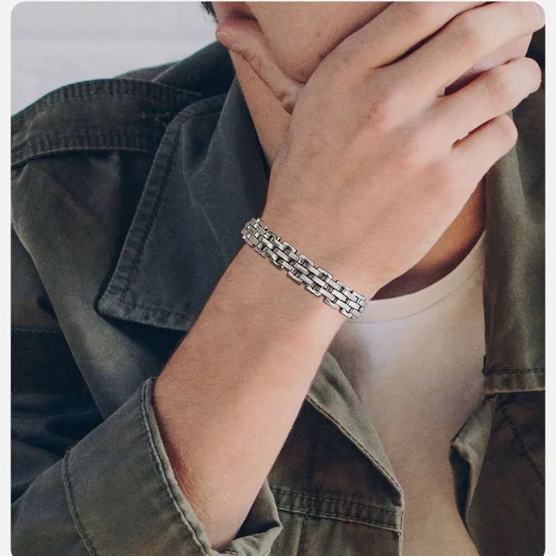 Silver watchband-link bracelet worn on the wrist of a man in an olive green jacket, resting his hand near his chin.