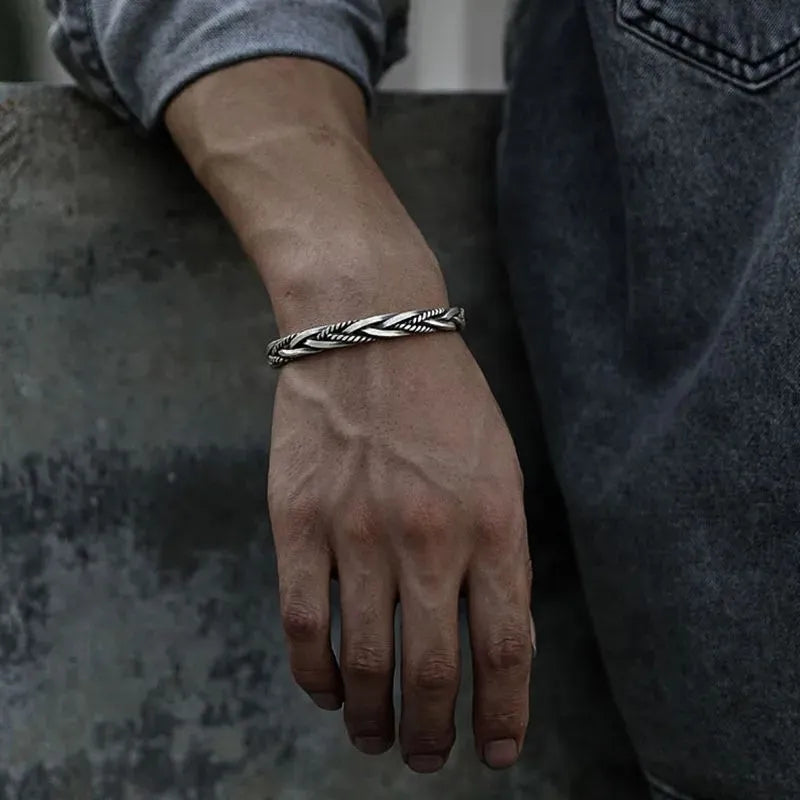 Silver twisted cuff bracelet worn on the wrist, resting on a stone ledge, paired with a denim jacket.