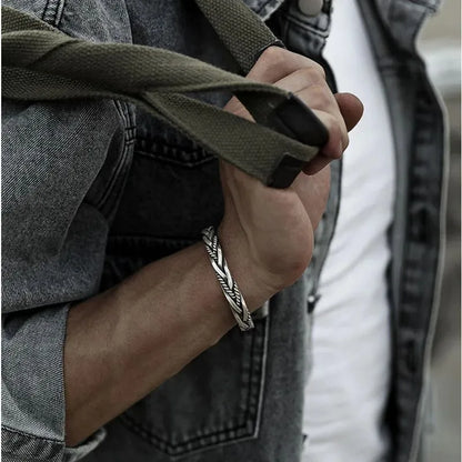 Silver twisted cuff bracelet worn on the wrist, hand gripping a green canvas bag strap, denim jacket over a white shirt.