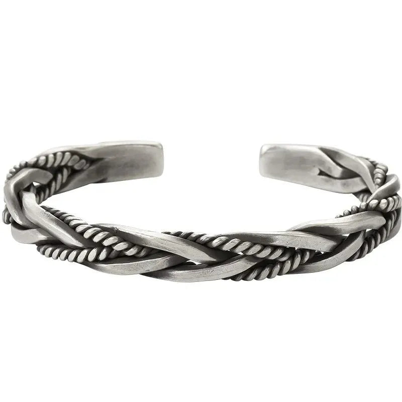 Silver open-cuff bracelet with a braided rope-and-flat-band twist pattern, laid on a plain white background.
