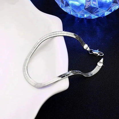 Silver flat blade chain bracelet draped on a white bust-shaped display prop, with a blue faceted crystal ball in the background.