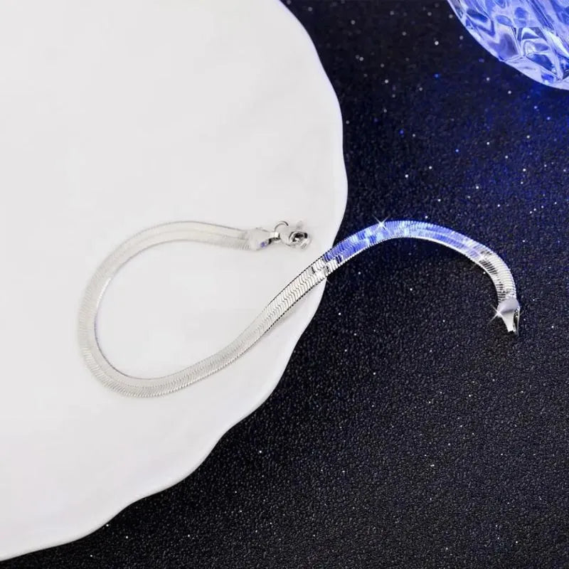 Silver flat blade chain bracelet draped over the edge of a white bust-shaped display prop, against a dark starry background with a blue crystal ball.