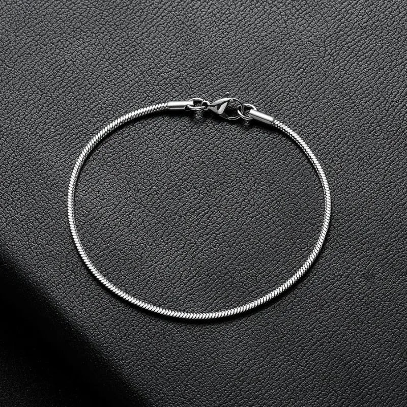 Silver snake chain bracelet laid in a circle on a black leather surface, showing the lobster clasp.