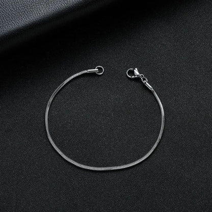 Silver snake chain bracelet shown open, laid in an oval on a black leather surface with a dark leather book prop.