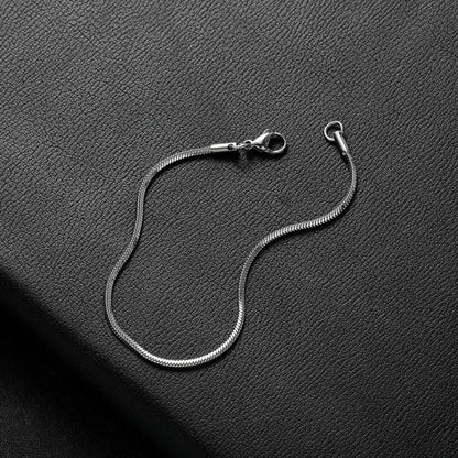 Silver thin snake chain bracelet shown open and unclasped, laid loosely on a black leather surface.