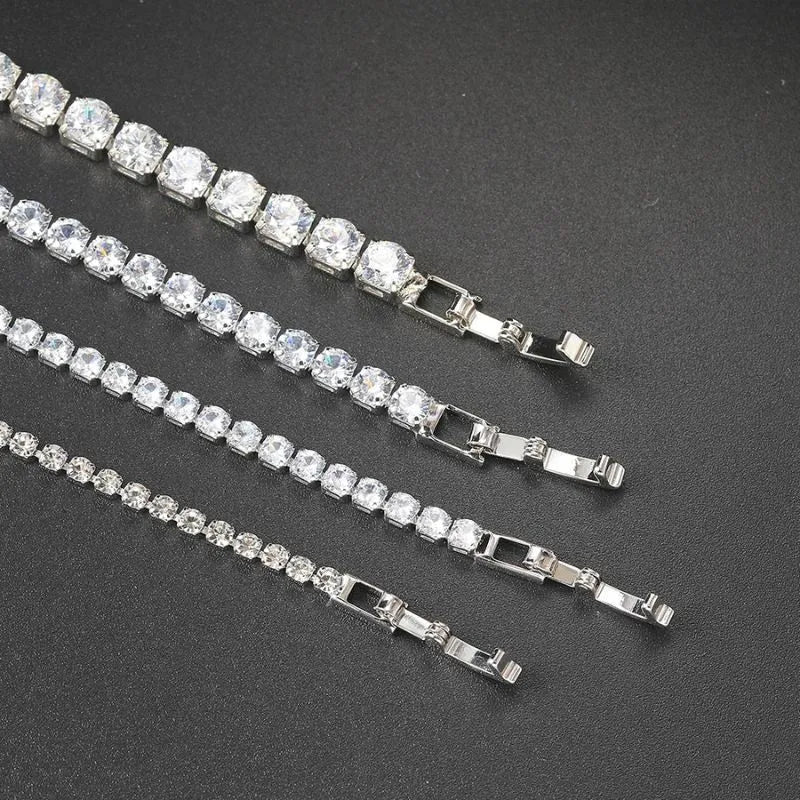 Four silver tennis bracelets of different stone sizes laid diagonally with their clasps visible, on a dark textured surface.