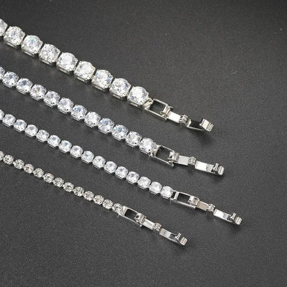 Four silver tennis bracelets of different stone sizes laid diagonally with their clasps visible, on a dark textured surface.