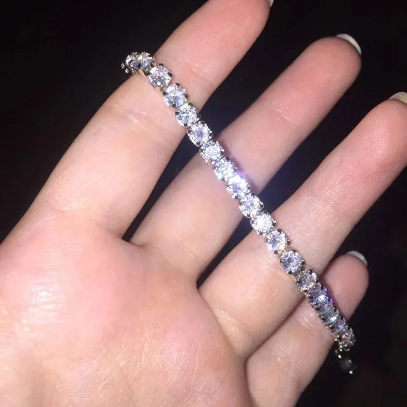 Silver tennis bracelet worn across the fingers to display its sparkle, against a black background.