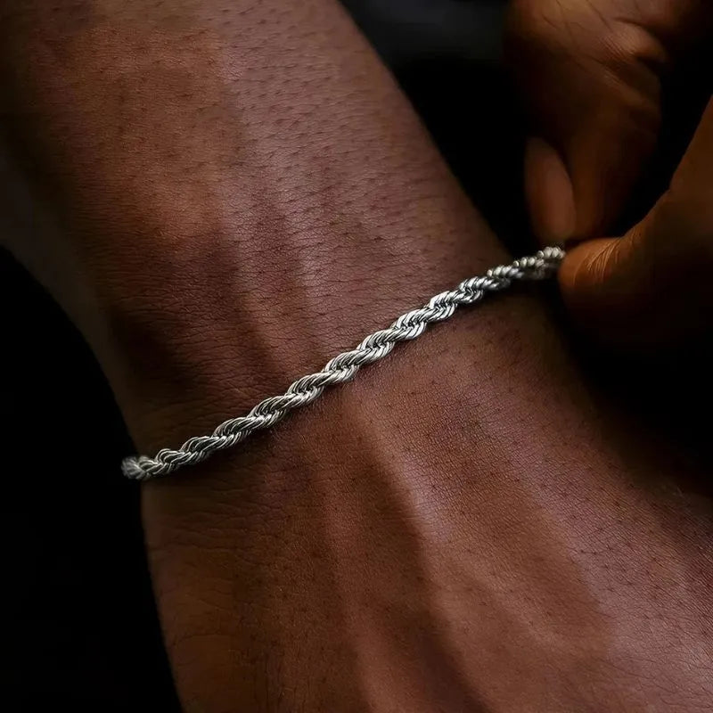 Close-up of the silver twisted rope chain bracelet worn on the wrist in dark, moody lighting, with a hand adjusting the clasp.