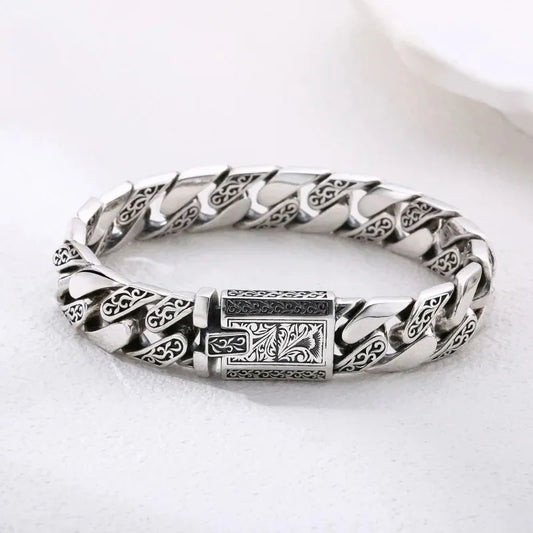 Engraved silver Cuban-link bracelet laid in an oval on a plain white background.