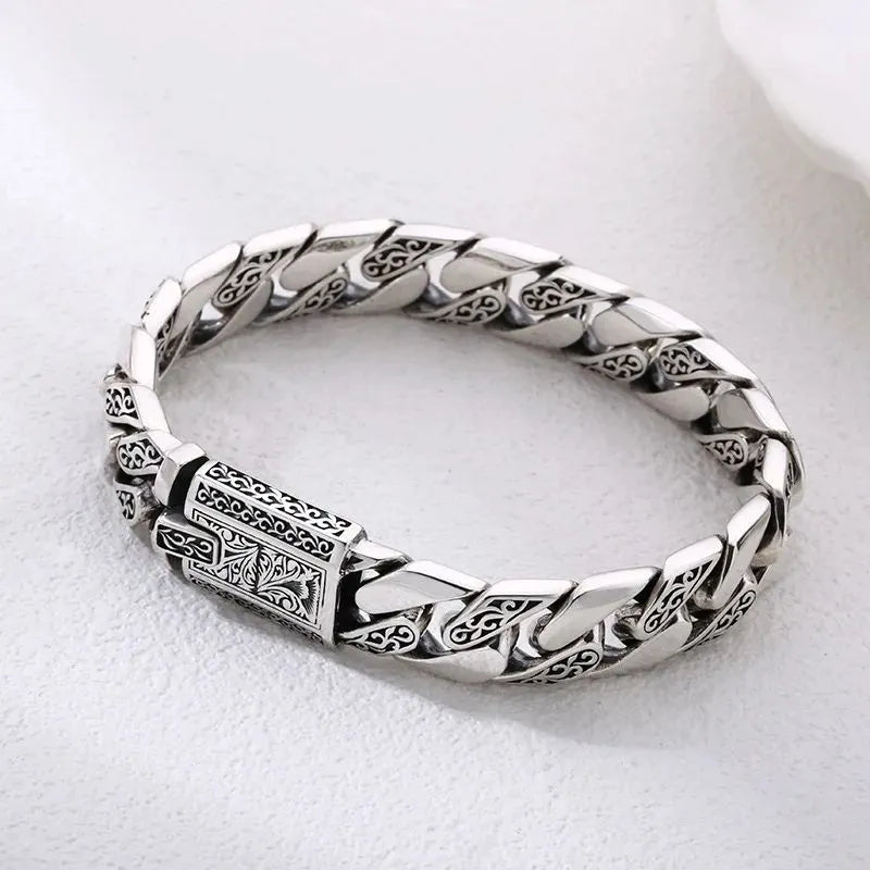 Engraved silver Cuban-link bracelet laid in an oval on a plain white background.