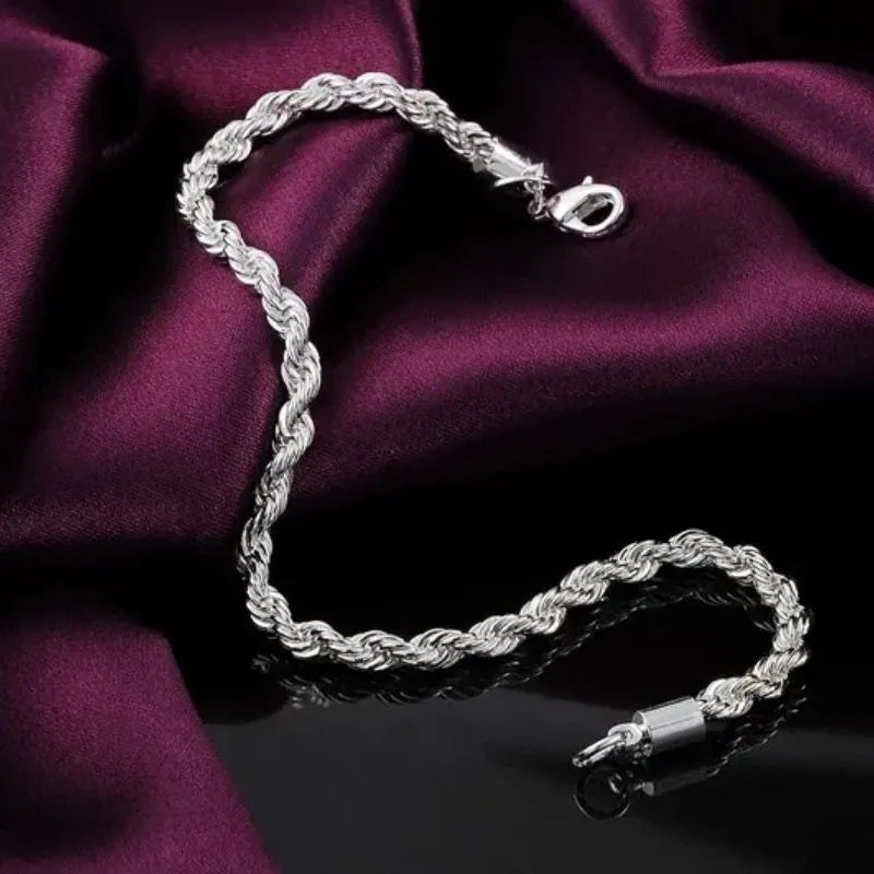 Silver twisted rope chain bracelet draped diagonally on dark wine-colored satin fabric, with a reflective black surface below.
