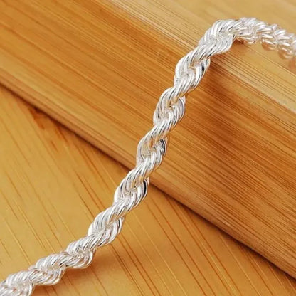 Close-up of the silver twisted rope chain's texture, resting on a wooden surface with a wooden block prop.