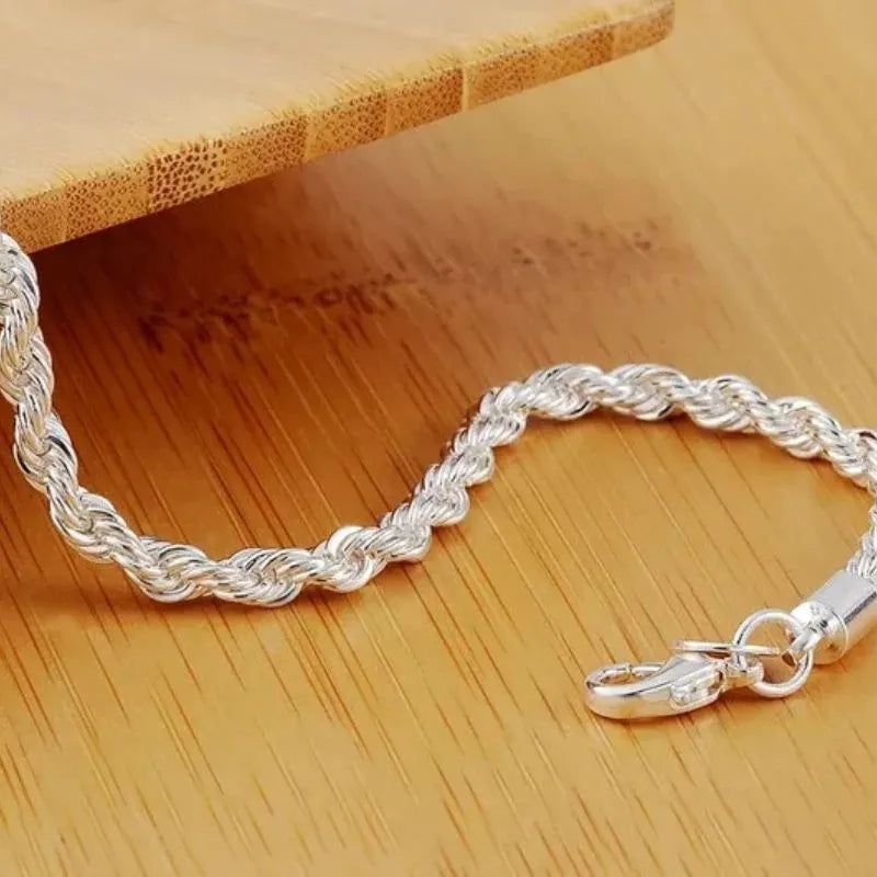 Silver twisted rope chain bracelet laid diagonally on a wooden surface, showing the lobster clasp, with a wooden block prop.