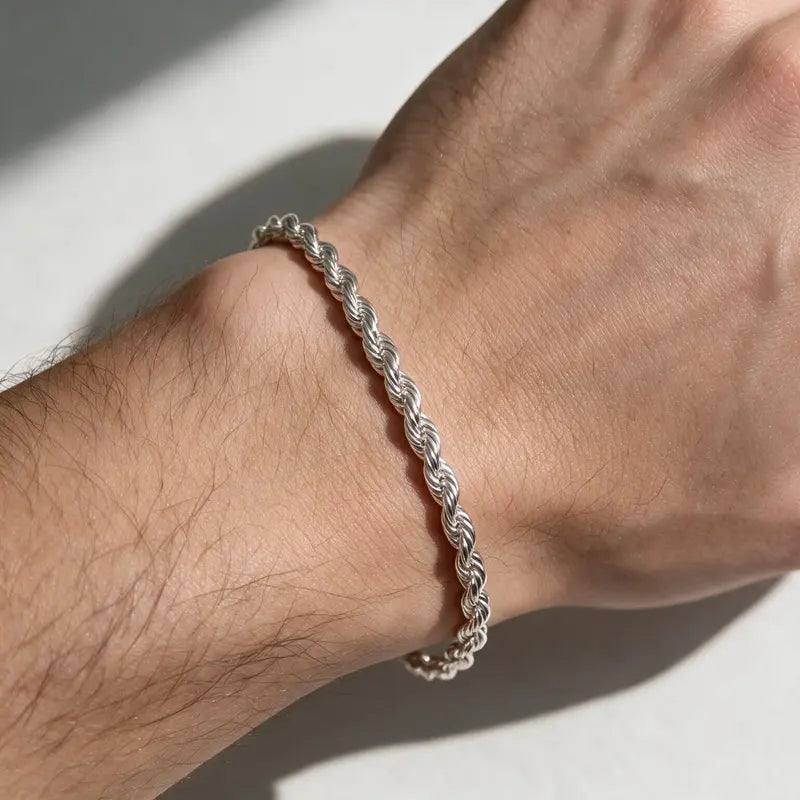 Silver twisted rope chain bracelet worn on a man's wrist, close-up in natural sunlight.