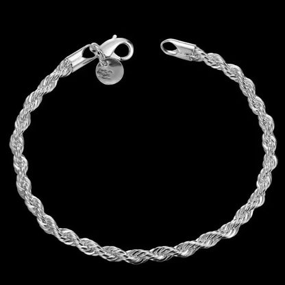 Silver twisted rope chain bracelet laid in a circle on a black background, with the lobster clasp and round tag charm visible.