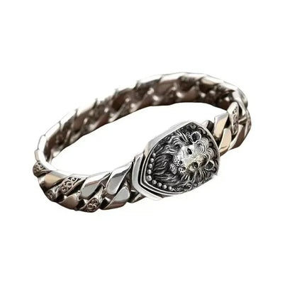Silver Cuban-link bracelet with a sculpted lion-head shield centerpiece, laid in an oval on a plain white background.