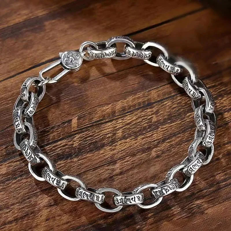 Silver mantra-engraved link bracelet laid in an oval on a wooden surface, with the clasp shown open.