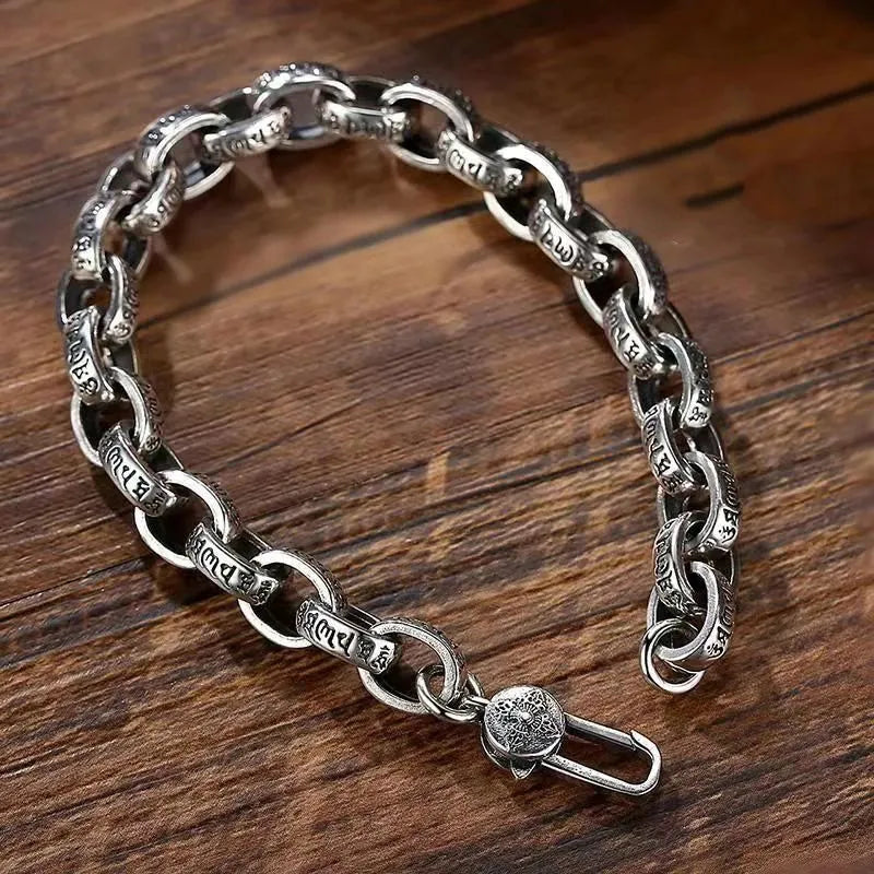 Silver mantra-engraved link bracelet laid open in an S-shape on a wooden surface, showing the clasp.