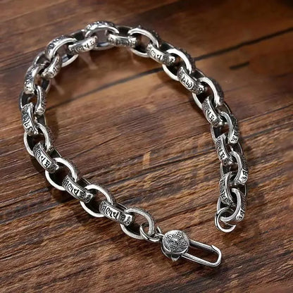 Silver mantra-engraved link bracelet laid open in an S-shape on a wooden surface, showing the clasp.