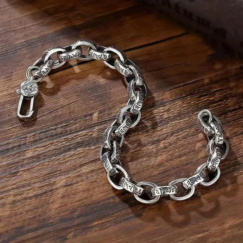 Silver mantra-engraved link bracelet laid open in a curved shape on a wooden surface, showing the clasp.