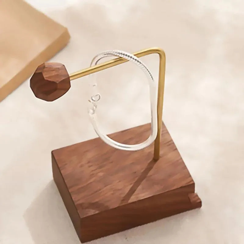Silver snake chain bracelet displayed on a small brass-and-wood jewelry stand with a decorative wooden bead counterweight.