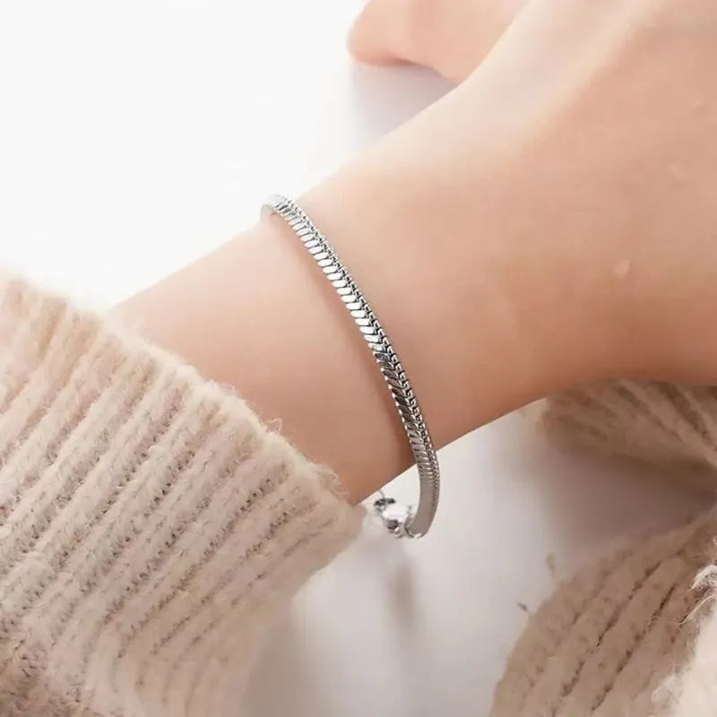 Close-up of the silver snake chain bracelet worn on the wrist, paired with a cream knit sweater sleeve.