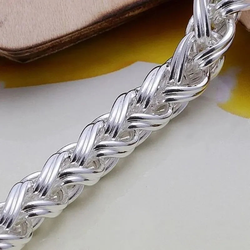 Extreme close-up of the silver wheat-chain bracelet's woven texture, propped against a leather-like surface.