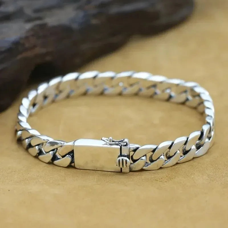 Close-up of the silver Cuban-link bracelet's polished links, laid on a tan suede surface with a dark rock prop.