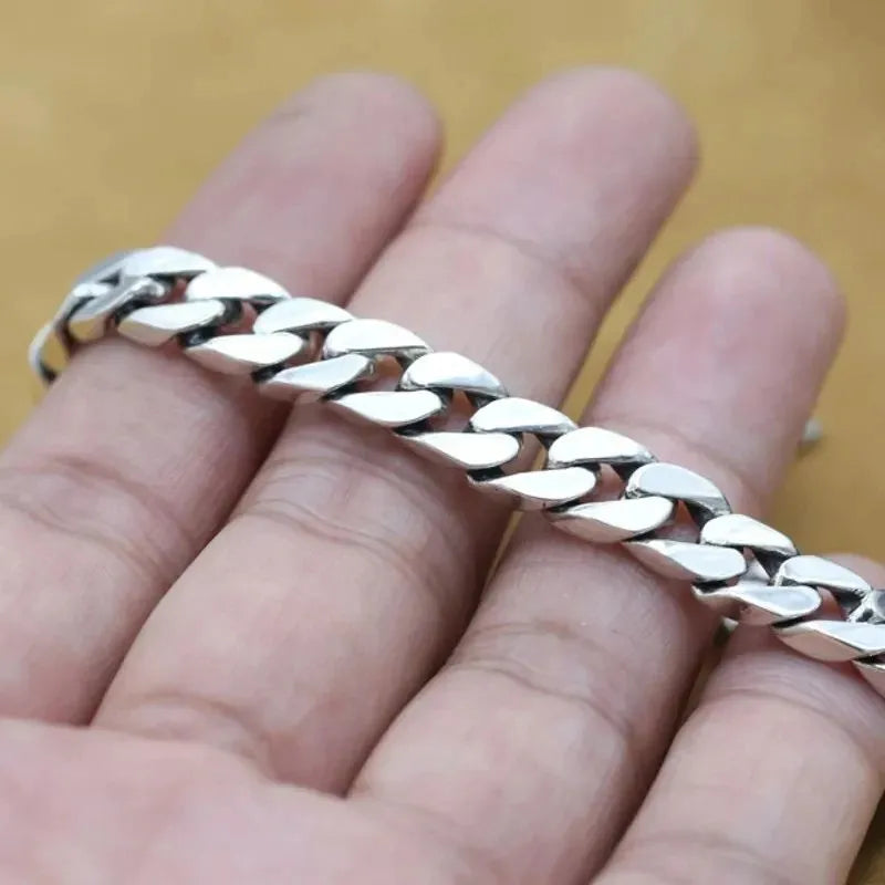 Silver Cuban-link bracelet draped across the fingers of an open hand, close-up against a tan background.