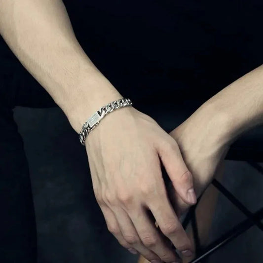 Silver Cuban-link bracelet worn on the wrist with arms crossed, against a black clothing background.