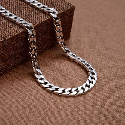 Silver Cuban-link bracelet draped in a loop over a small fabric-covered box, on a brown woven fabric surface.