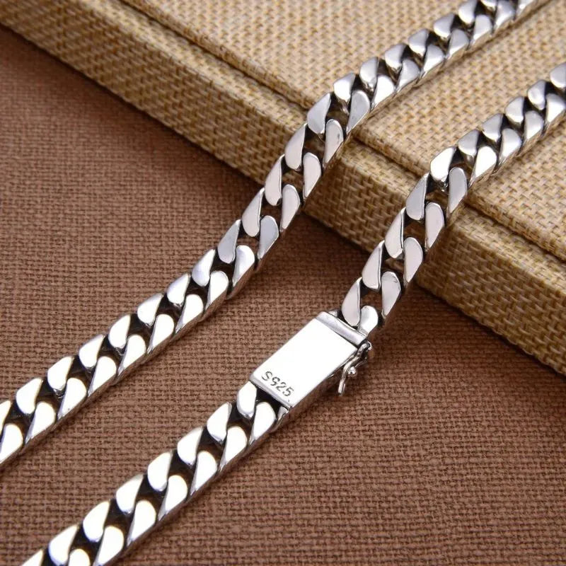 Close-up of the 'S925'-stamped clasp on the silver Cuban-link bracelet, draped over a woven fabric box.