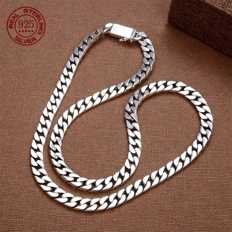 Long silver Cuban-link chain coiled on a brown surface, with a wooden box prop and a red 'Real Sterling Silver 925' hallmark stamp visible.