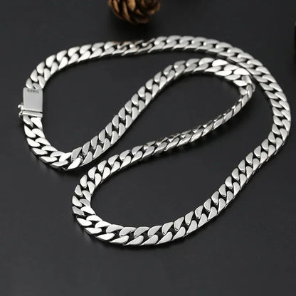 Long silver Cuban-link chain coiled on a dark surface, with a pinecone-shaped prop and an 'S925' stamp visible on the clasp.