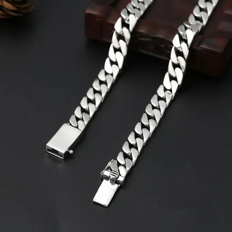Long silver Cuban-link chain shown open and unclasped, draped over a dark wooden box on a dark surface.