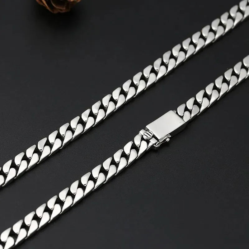 Close-up of the clasp on the long silver Cuban-link chain, against a dark surface with a pinecone-shaped prop.