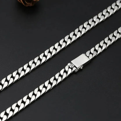 Close-up of the clasp on the long silver Cuban-link chain, against a dark surface with a pinecone-shaped prop.