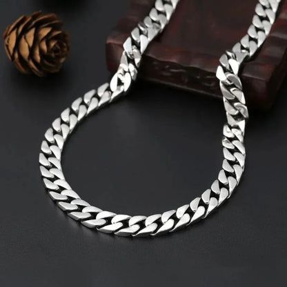 Long silver Cuban-link chain looped over a dark wooden box, with a pinecone-shaped prop on a dark surface.