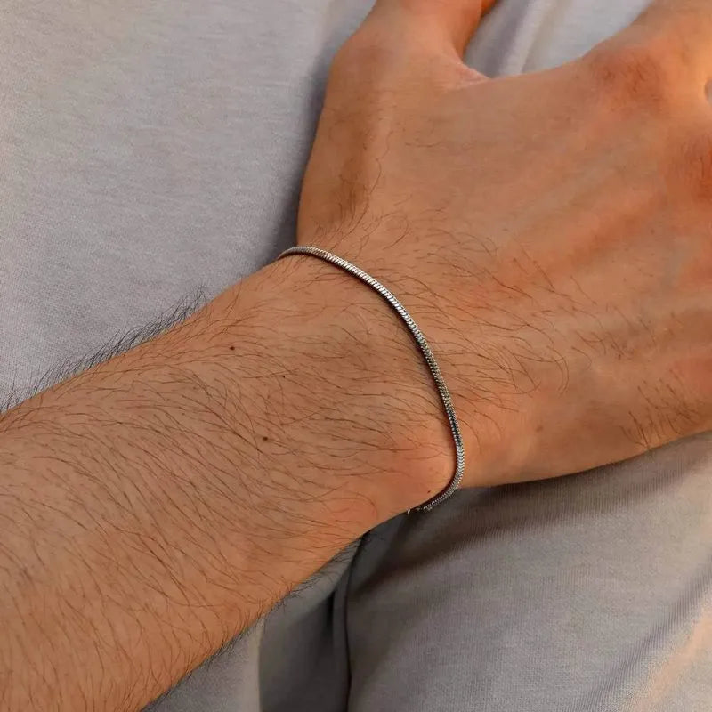 Single silver snake chain bracelet worn on the wrist, against a light grey shirt background.