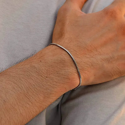 Single silver snake chain bracelet worn on the wrist, against a light grey shirt background.