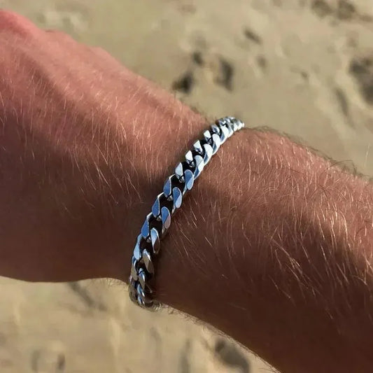 Silver Cuban chain bracelet worn on the wrist outdoors on a sunlit sandy beach.