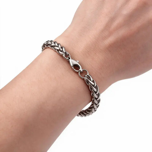 Silver stainless steel wheat chain bracelet worn on wrist, white background